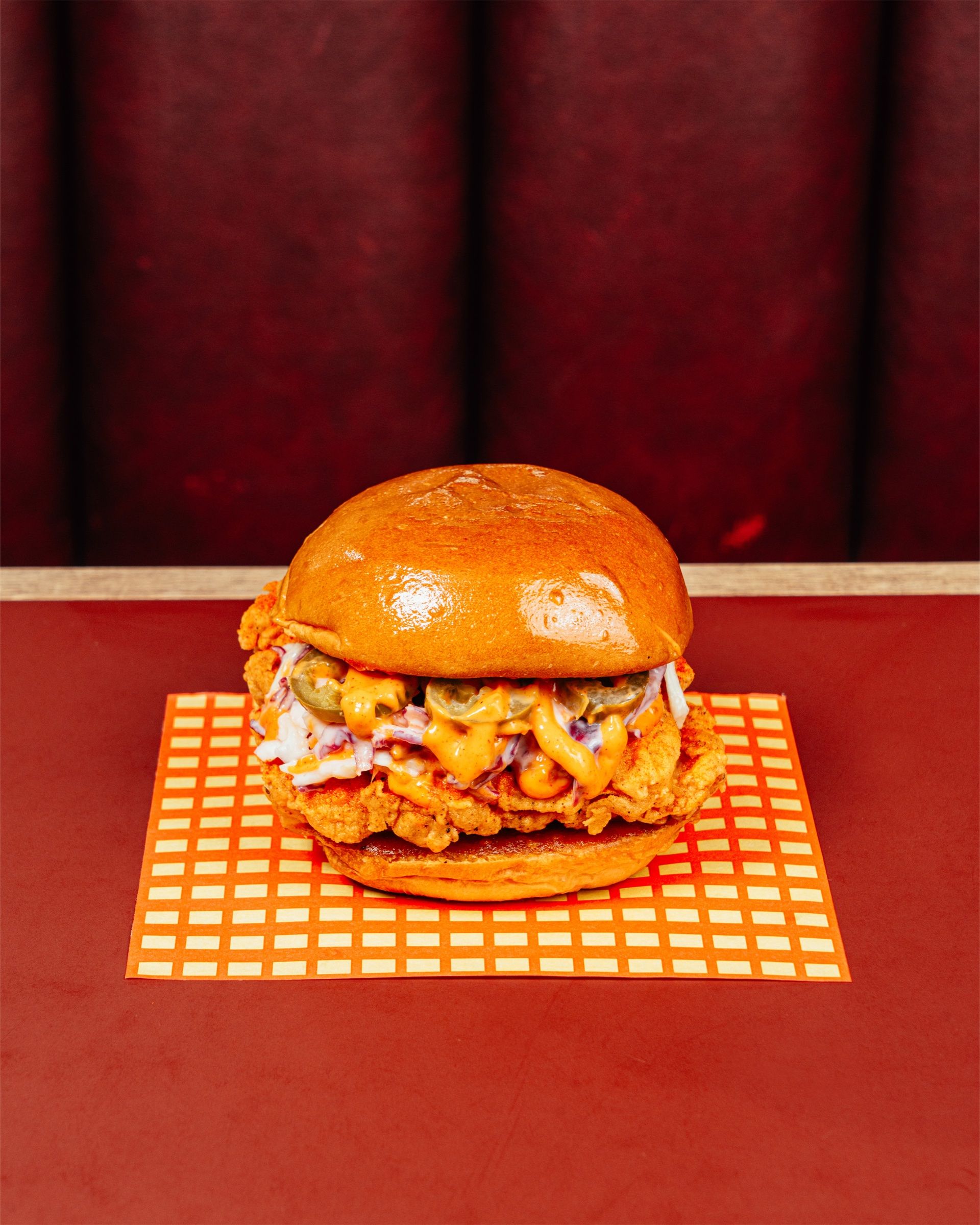 The Motherclucker sandwich with house slaw on checked paper, on a red diner table