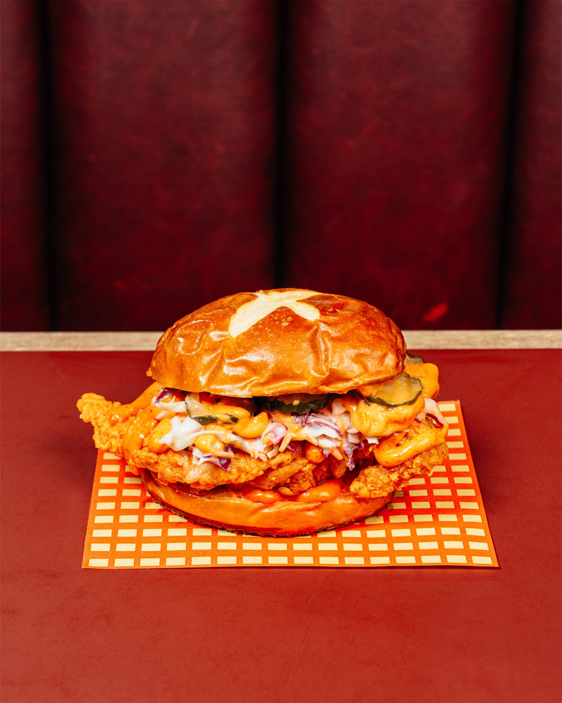 The Nashville sandwich on a pretzel bun, on checked paper on a red diner table