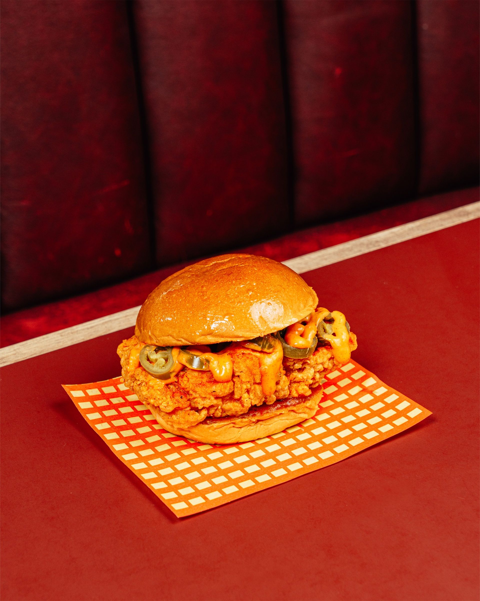 The O.G. Sandwich with jalapeño pickles on checked paper, on a red diner table