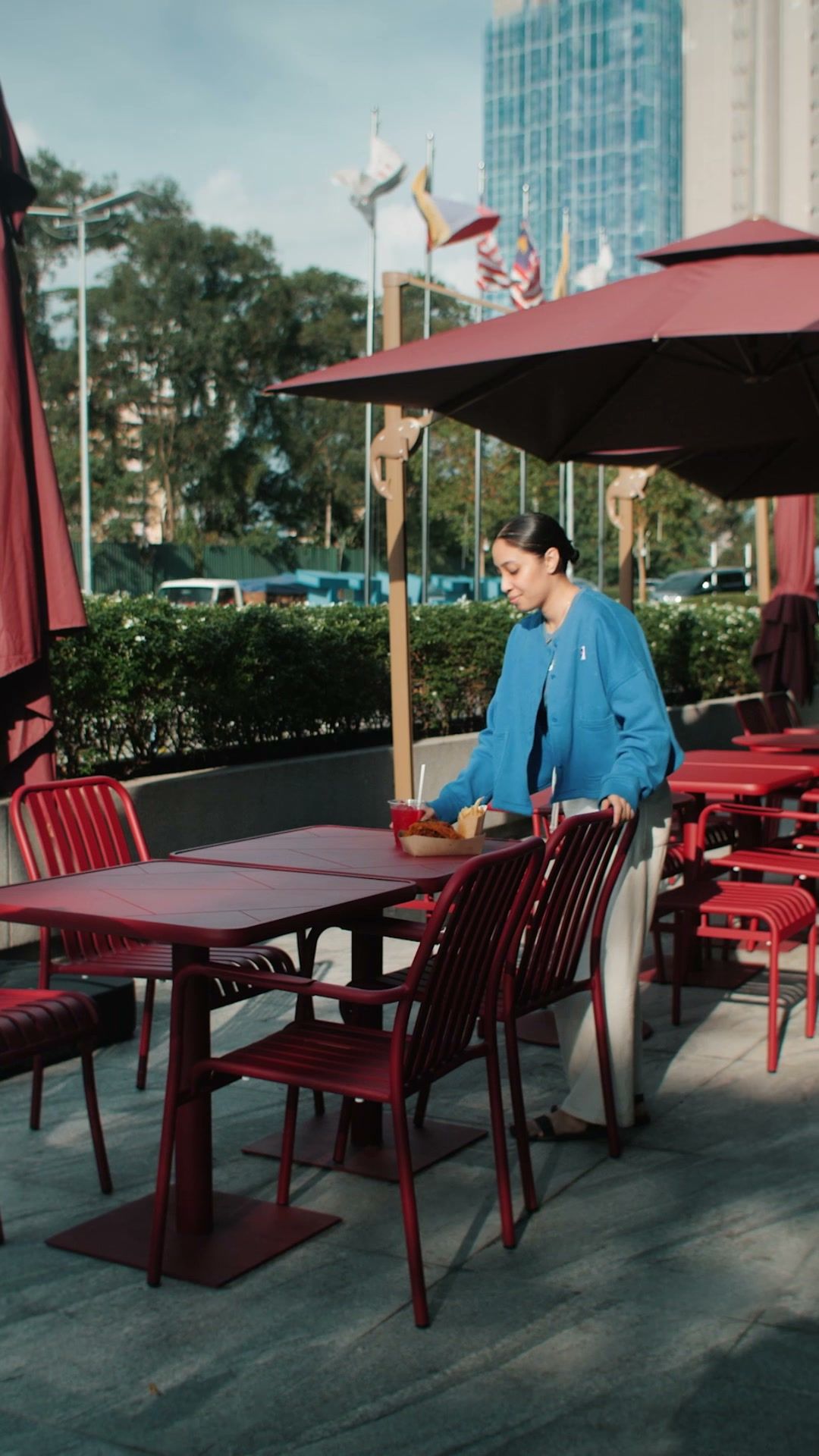 A guest setting her food down at a red table on The MET’s terrace, under the umbrellas and the tower