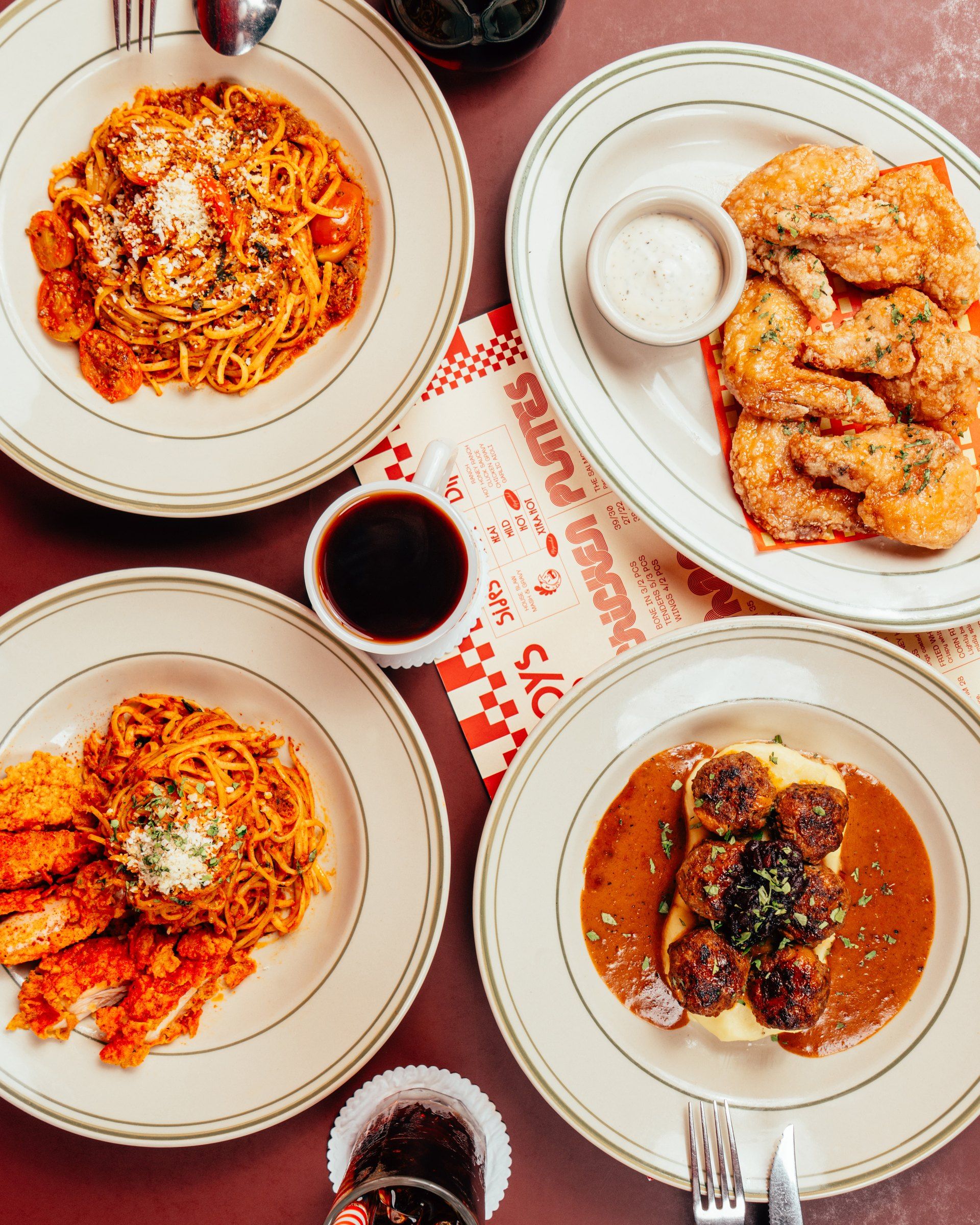 A diner table from above — two linguines, wings, swedish meatballs and coffee on the fowlboys placemat