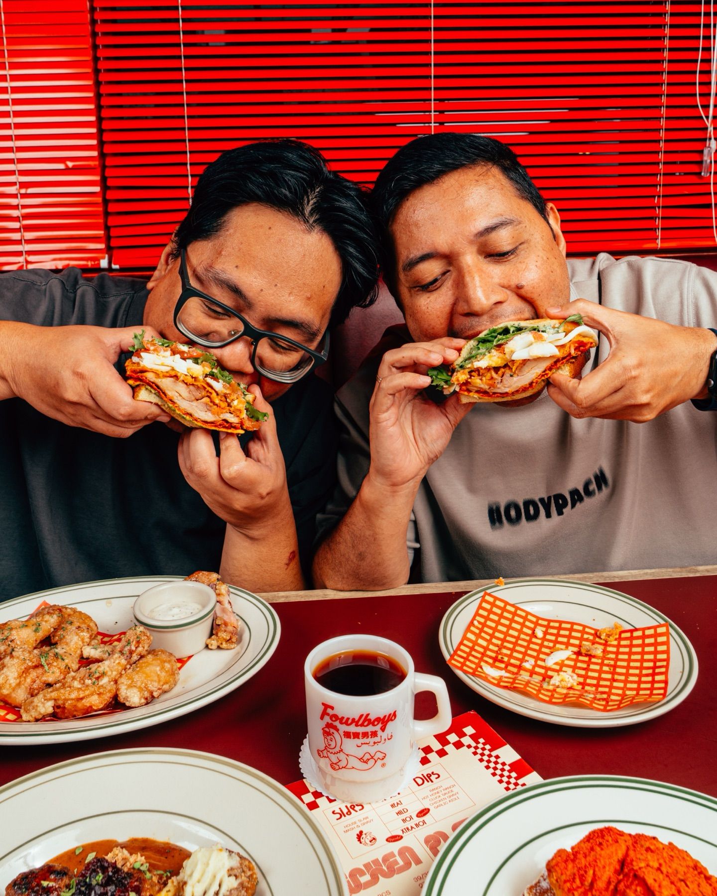Two guys laughing mid-bite over sandwiches