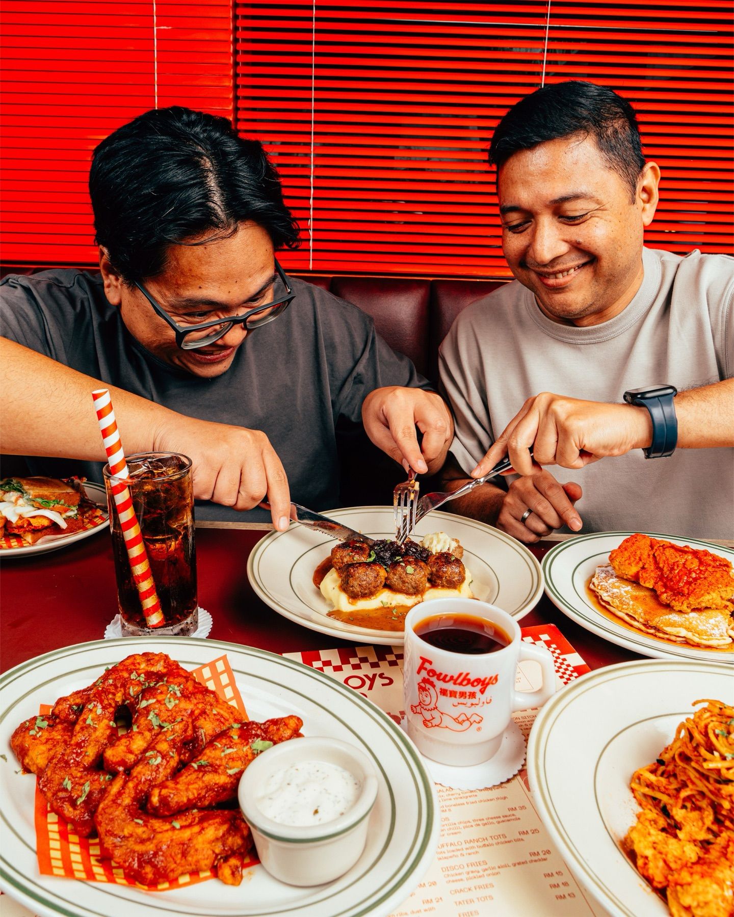 Two friends cutting into a shared plate in a booth, hot wings in front