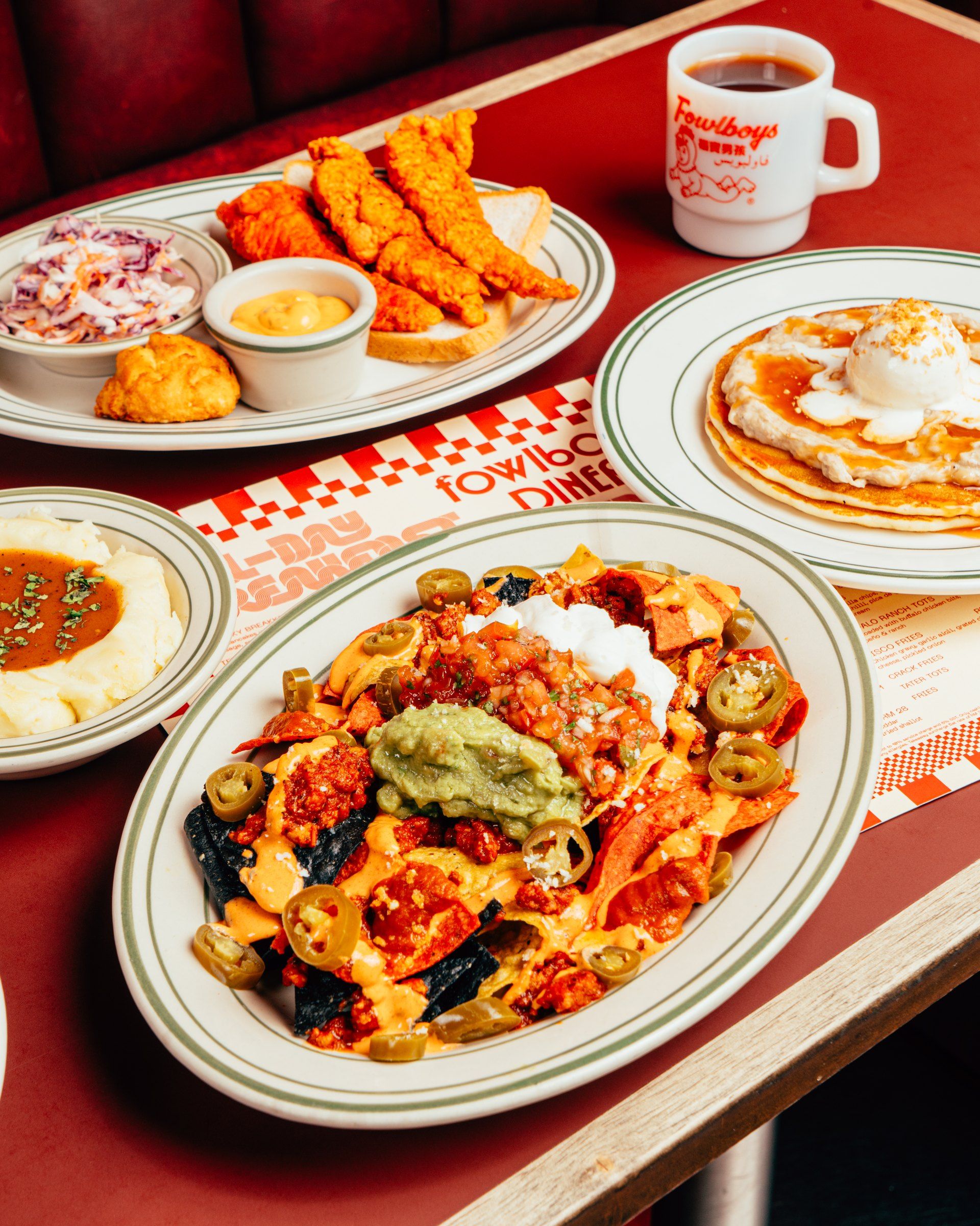 Loaded nachos up close, with tenders, slaw, mash, pancakes and a fowlboys mug around them