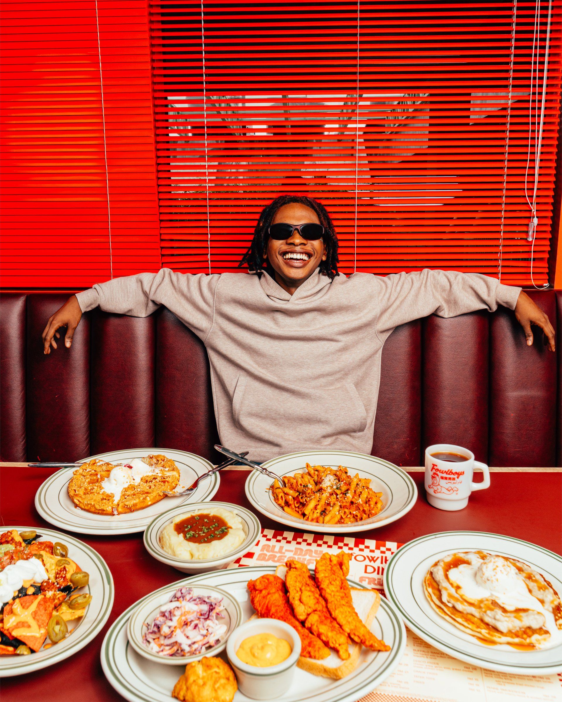 A diner in sunglasses leaning back in a red booth behind a full table